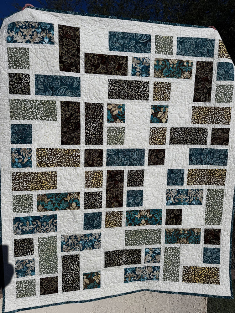 Quilt with square blocks of brown, green, and aqua on a cream background.